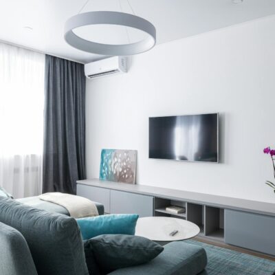 Modern interior of cozy living room in gray colors with TV on wall and gray cabinet below with blooming orchid flower